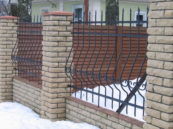 Незыблемый и изысканный кованый забор с кирпичными столбами.
